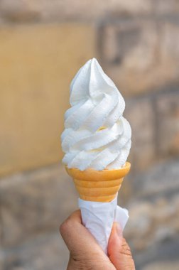 Soft whipped vanilla ice cream with chocolate stick in waffle cone in hands