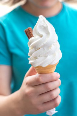 Soft whipped vanilla ice cream with chocolate stick in waffle cone in hands