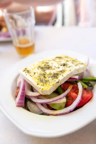 Traditional Greek Salad served in tavern, traditional greece food with Aegean sea as background. Tomatoes, cucumber, onions, olives, peppers, cappers and olive oil