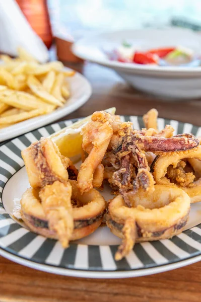 Traditional Greek crispy squids or calamari rings served with french fries in tavern, traditional greece food