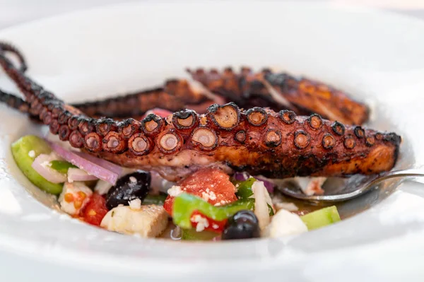 Traditional Greek Salad served with Fried Octopus in tavern, traditional greece food. Tomatoes, cucumber, onions, olives, peppers, cappers and olive oil