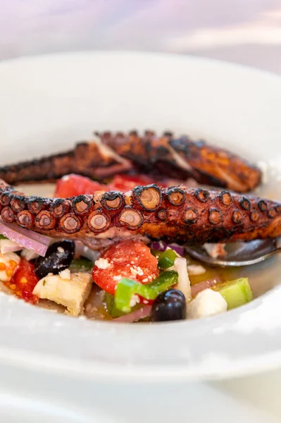 Traditional Greek Salad served with Fried Octopus in tavern, traditional greece food. Tomatoes, cucumber, onions, olives, peppers, cappers and olive oil