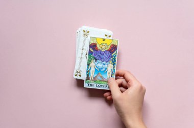 London, UK: 14 October, 2022: The 6 Major Arcana - The Lovers Tarot Card of Rider Waite deck in hand on pink background clipart