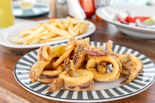 Traditional Greek crispy squids or calamari rings served with french fries in tavern, traditional greece food