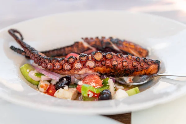 Traditional Greek Salad served with Fried Octopus in tavern, traditional greece food. Tomatoes, cucumber, onions, olives, peppers, cappers and olive oil