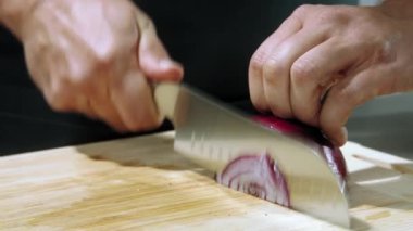 Şef soğanları doğradı, soğanları yakın plan doğradı, soğanları doğradı, soğanları yavaş çekimde doğradı, soğanları arka plan tahtasındaki bıçakla temizledi.