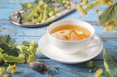 Mavi arka planda ıhlamur çiçekleri olan bir fincan bitki çayı.