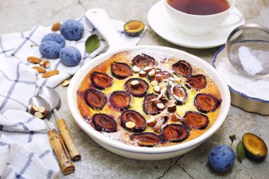 Damson Blue Pum Clafoutis (turta), krema şekeri ve badem sosu, açık arkaplanda Fransız mutfağı.