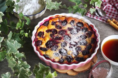 Mavi erik tohumu (flan), kremalı şeker sosu ve bir fincan çay, ahşap zemin üzerinde Fransız mutfağı.