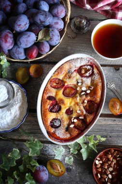 Damson mavisi erik pudingi (turta) ve bir fincan çay, krema şekeri ve badem sosu, ahşap zemin üzerinde Fransız mutfağı. Kırsal biçim, üst görünüm