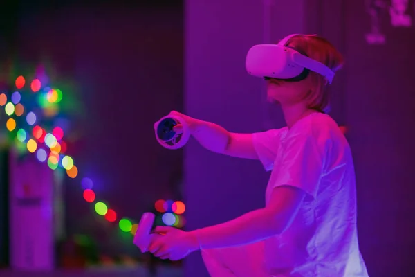 Smiling woman playing game with controls in virtual reality. Future technology concept. Colorful neon lights.