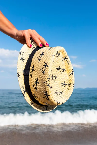 Woman holding straw sun hat at sunny beach at sea .Travel and fashion concept