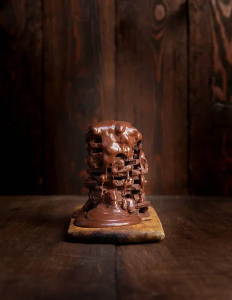 Melted hot chocolate dripping over a pile of chocolate bars on a rustic wooden table