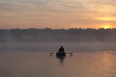 Sabahın köründe gölde balık tutmak. Şafak vakti, pembe bir sis içinde bir teknede yüzen insan.