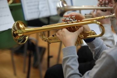 Müzisyen bir trompetçinin elinde altın trompet. Okul caz grubu konserinin arka planında yakın plan görüntüsü.