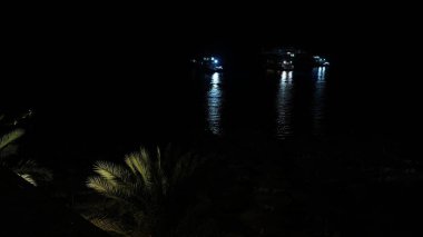 Gece körfezde duran bir gemi. Siyah suya yansıyan parlak bir ışık.