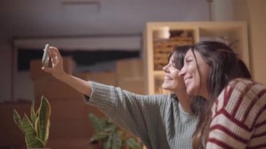 Kadın bir çift taşınma sırasında yeni evlerinde selfie çekiyor. Mutlu arkadaşlar fotoğraf çeker ve akıllı telefon kullanır..