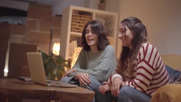 女性のカップルは移動中に新しい家にビデオ通話を行います。幸せな友人は家族と喜びを共有し、ラップトップで電話をかける. — ストック動画