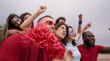 Farklı ırktan ve yaşlardan bir grup insan tribünde futbol maçını izliyor. Erkekler ve kadınlar takım elbiseleriyle birlikte mutlu bir şekilde kutlarlar..