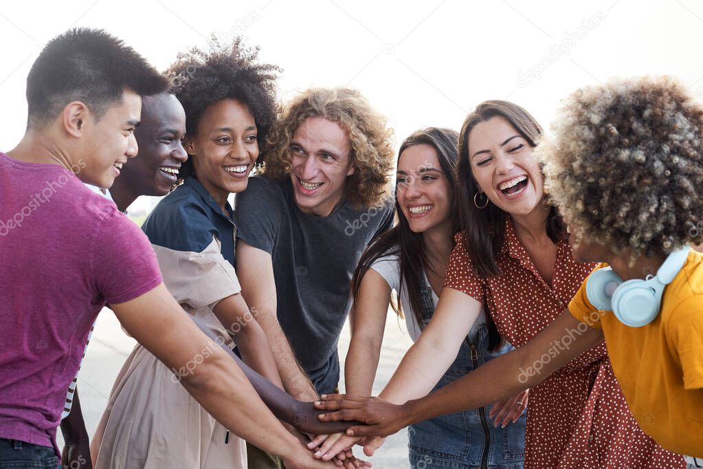 Friends of different ethnicities stacking hand and looking at each other. Group of people having fun and celebrating. Concept of friendship, happiness, joy.