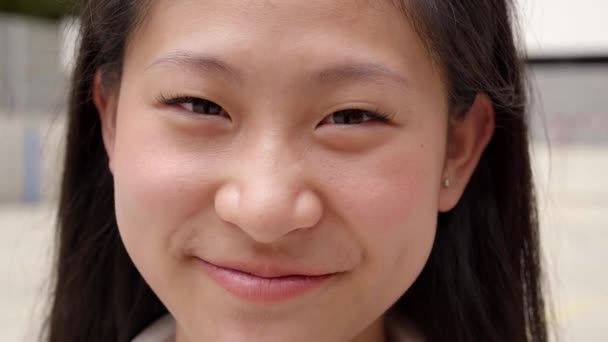 Adolescente chino sonriendo feliz. Primer plano retrato de alegre chica asiática mirando a la cámara de pie al aire libre sobre fondo borroso. — Vídeo de stock