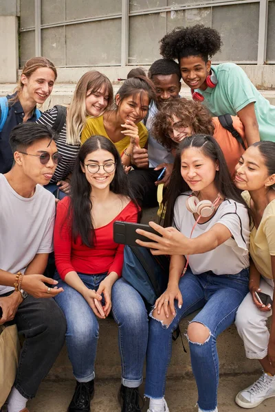 Κάθετη φωτογραφία ομάδας πολυεθνικών φοιτητών που βγάζουν selfies με κινητό τηλέφωνο. Έφηβοι χρησιμοποιούν ένα έξυπνο τηλέφωνο και διασκεδάζουν μαζί. — Φωτογραφία Αρχείου