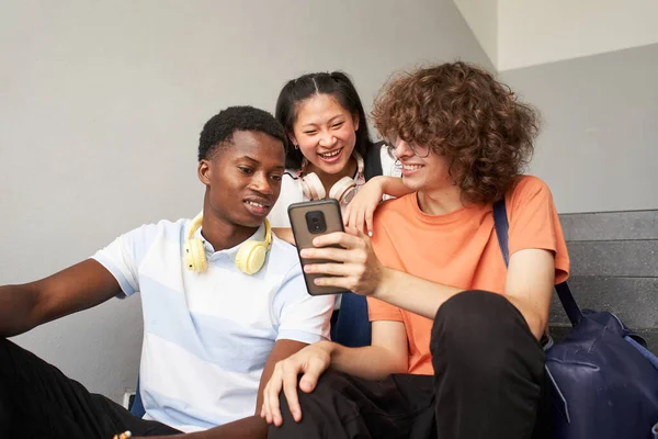 Grupa nastoletnich studentów różnych grup etnicznych siedzących na zewnątrz na schodach uniwersytetu przy użyciu telefonu komórkowego. — Zdjęcie stockowe