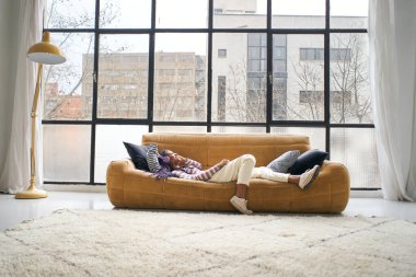 Modern ve parlak bir evde genç bir kadın, bir kanepeye uzanıp kulaklıkla müzik dinliyor ve dans ediyor..