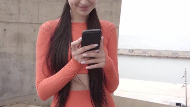 De cerca mujer sonriente en ropa deportiva usando el teléfono al aire libre. — Vídeos de Stock