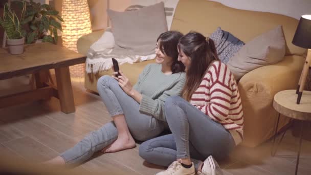 Feliz pareja de amigas arrendatarias inquilinas sentadas en un sofá tomando selfie. Videollamada en casa, tecnología de dispositivos en línea. — Vídeos de Stock