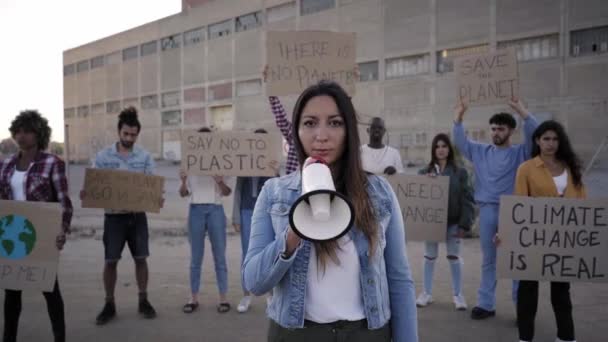 Al rallentatore di una donna con un megafono che guida una protesta guardando la telecamera. Le persone che sostengono il cambiamento climatico sono dei veri e propri striscioni. — Video Stock