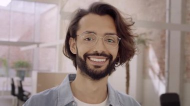 Ofiste durup kameraya bakan gülümseyen genç bir iş adamının portresi.