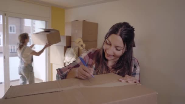 Крупный план портрета молодой женщины, пишущей на картонных коробках, маркирующих их за перемещение. Новая жизнь в новом доме переселения. — стоковое видео