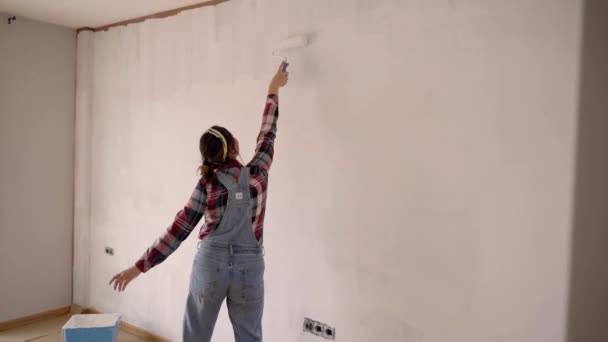Une joyeuse dame excitée chante en dansant contre un mur mi-coloré dans un nouvel appartement après le déménagement. Relooking et concept amusant. — Video