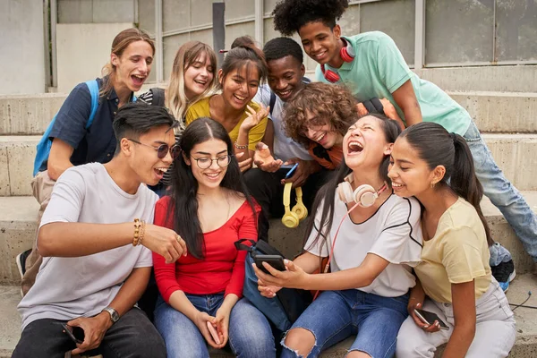 Πολυεθνική ομάδα μαθητών που χρησιμοποιούν κινητό τηλέφωνο και γελούν. Έφηβοι που χρησιμοποιούν ένα έξυπνο τηλέφωνο, σερφάρουν στο διαδίκτυο. Διασκεδάζουμε μαζί.. — Φωτογραφία Αρχείου