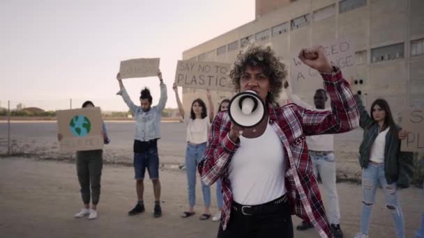 Mouvement lent d'une femme menant une manifestation criant avec un mégaphone regardant la caméra. Personnes portant des bannières sur le changement climatique. — Video