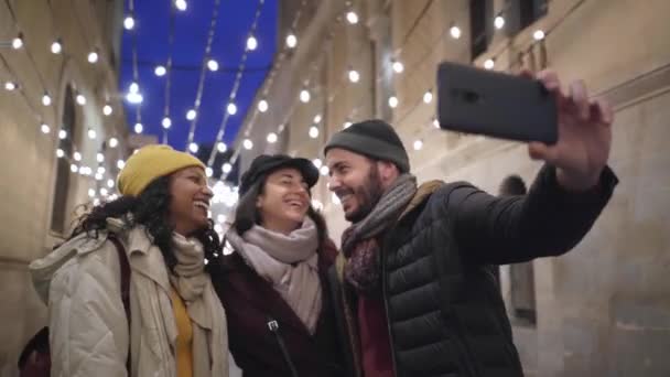 Grupo de amigos felices tomando una selfie con smartphone en las vacaciones de invierno en la ciudad. La gente sonriendo a la cámara con sombrero y cara de cicatriz. — Vídeos de Stock
