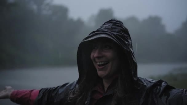 Young girl in raincoat smiles and laughs in the rain.View from above portrait of girl looking at sky enjoying raindrops falling on face while standing in nature. — Video Stock