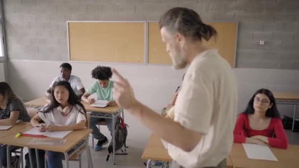 Multinational high school students listen to the teacher teaching. Several teenage students learning. Tracking side view. — Stockvideo