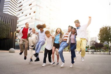 Carefree happy friends jumping in the street. Multiethnic group of young teenagers having fun together outdoors.