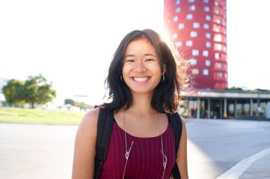 Portrait of a beautiful young woman in Barcelona. She is Asian, on her early twenties, brunette with long hair. Looking at camera and smiling. Smart casual clothes, urban background 