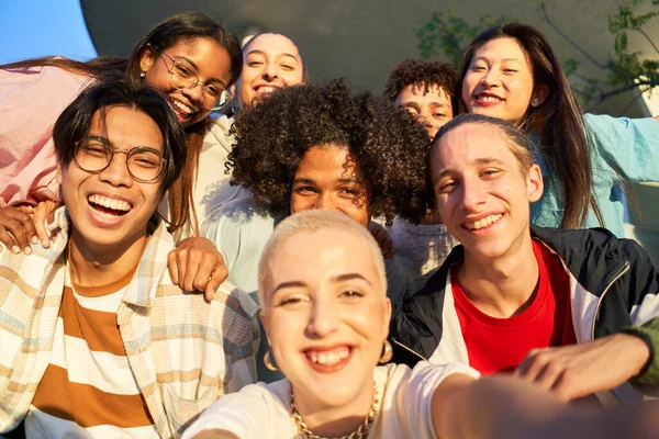 笑着自拍一百周年快乐。在大学校园里,一群多种族的学生聚在一起.重点是背景中的人 — 图库照片