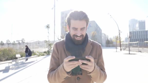 Joven empresario guapo exitoso usando el teléfono mientras camina al aire libre en el centro financiero en una ciudad — Vídeos de Stock