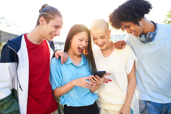 Gen Z jóvenes estudiantes utilizando teléfonos inteligentes y redes sociales juntos. Personas multirraciales divirtiéndose juntas viendo pantallas de teléfonos celulares al aire libre. — Foto de Stock