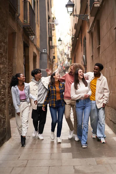 Foto vertical de un grupo de jóvenes amigos felices caminando por la calle de la ciudad. Estudiantes sonrientes riendo y divirtiéndose juntos — Foto de Stock