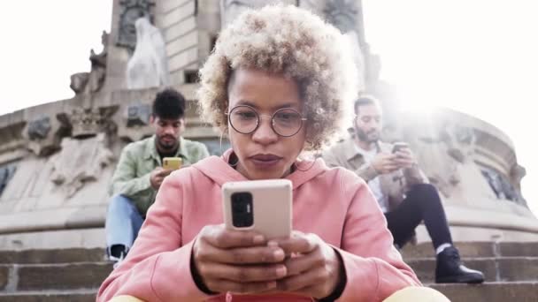Grupo de pessoas usando telefone com cara séria e ignorando uns aos outros. Uma mulher se concentrou em seu celular sentado em uma escada em uma cidade. Tecnologia viciados conceito. — Vídeo de Stock