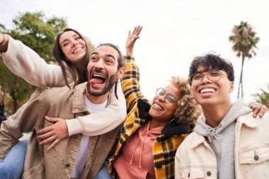 Farklı kültürlerden ve ırklardan mutlu arkadaşlar dışarıda selfie çekiyorlar. Neşeli insanlar eğleniyor