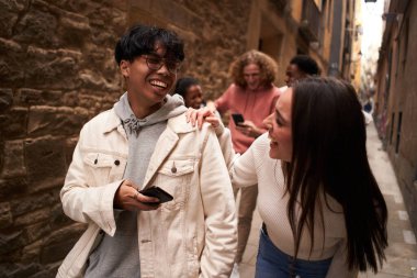 Bir grup mutlu arkadaş dışarıda yürürken ve gülerken telefon kullanıyor..