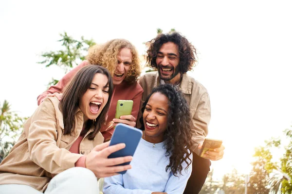 Boldog barátok néz képernyő mobiltelefon egy meglepett arc és mosolygós. Fiatal felnőttek okostelefont használnak és jól érzik magukat. — Stock Fotó