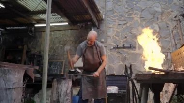 Sert orta yaşlı adam sıkı çalışıyor. Demirci, örs çekiciyle erimiş metali elle dövüyor. Bir işçiyle atölye çalışması..
